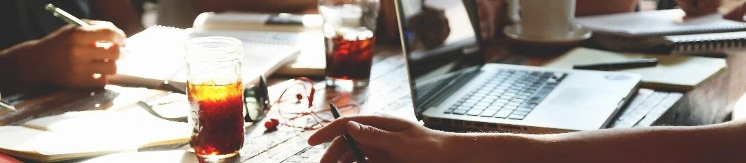 A table where three people have been working, with documents and an open laptop